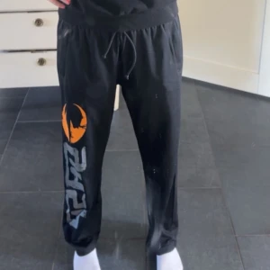 Svarta gasp byxor  - Säljer ett par svarta gasp byxor med ett coolt tryck i orange och vitt på ena benet. Byxorna har en bekväm passform med snörning i midjan och är perfekta för en avslappnad stil eller till träning!🥰