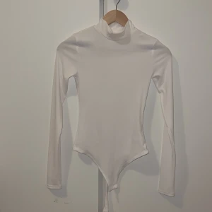 Vit polotopp från H&M - Säljer en stilren vit polotopp från H&M. Toppen är långärmad och har en tight passform, perfekt för lager-på-lager eller som den är. Materialet är mjukt och stretchigt för en bekväm känsla.