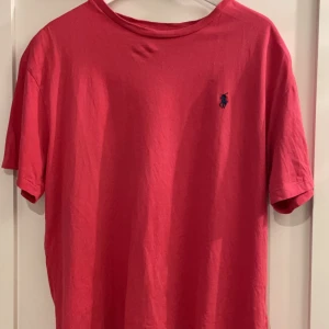 Röd t-shirt från Ralph Lauren - Snygg röd t-shirt från Ralph Lauren med klassisk logga på bröstet. Perfekt för en avslappnad stil. Tillverkad i mjukt material för extra komfort.