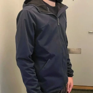 Marinblå softshell jacka från Sail Racing - Snygg marinblå jacka från Sail Racing med dragkedja och huva. Perfekt för vintern och våren med sin stilrena design och praktiska fickor. Jackan  är tillverkad i ett slitstarkt material. Den är storlek S