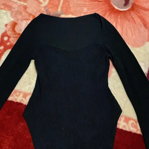 Svart ribbad klänning - Snygg svart ribbad tröja med långärmad design. Perfekt för en stilren look med en figurnära passform. Klänningen har en elegant och enkel stil som passar till många tillfällen.