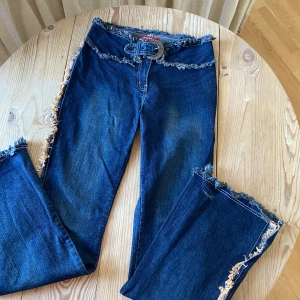 Blå jeans med fransdetaljer - Snygga blå 2000tals jeans från Miss Sixty med unika fransdetaljer längs sidorna och i midjan. De har en lågmidjad passform och ett medföljande bälte som ger extra stil. Lite western/cowboy stil! Slitsar längst ner på utsidan! Såå fina och unika! Storlek w 30 men skulle säga S/M! Stretchiga o sitter bekvämt! Midja 39cm innerben 80cm