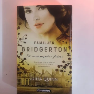 Familjen Bridgerton: Ett minnesvärt frieri - Boken 'Familjen Bridgerton: Ett minnesvärt frieri' av Julia Quinn är en del av den populära Bridgerton-serien. Omslaget har en bild av en kvinna och en herrgård i bakgrunden, med dekorativa blommor. Perfekt för dig som älskar romantiska berättelser.