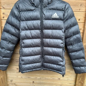 Svart dunjacka från Adidas - Adidas jacka i storlek M, (lite tight) knappt använd men lagat på ett ställe (SE BILD 3) syns knappt att de är lagat. 
