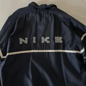 Nike vindjacka - Säljer denna assnygga vindjacka då jag inte använt den på över ett år. Skitsnygg, baggy, om du inte gillar den nedre delen kan man vika in den (jag brukade ha på mig den så).
