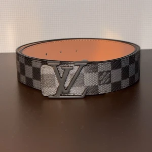 Rutig bälte - Snyggt bälte  med ett klassiskt rutigt mönster i svart och grått. Bältet har en stilren metallspänne. Perfekt för att ge en lyxig touch till din outfit.