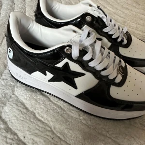 Svartvita sneakers från BAPE - Snygga svartvita sneakers från BAPE med den ikoniska stjärndesignen på sidan. Skorna har en glansig finish och klassisk snörning. Perfekta för en stilren look. Aldrig hittat användning för dom