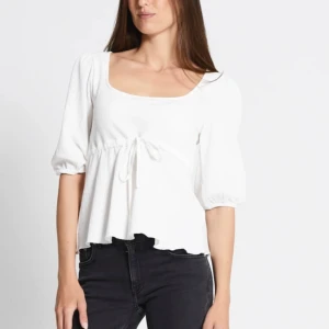 Vit blus med knytning - Säljer en söt vit blus med trekvartsärm och knytning framtill. Den har en lös passform och är perfekt för både vardag och fest. Materialet känns mjukt och bekvämt.