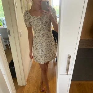 Blommig klänning  - Blommig ljus klänning från H&M i storlek S, men passar även som XS. Har resår baktill. Puffiga ärmar med knytning framtill. Endast använd 1 gång.