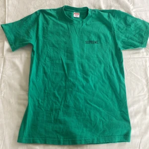 Grön Supreme t-shirt med 'Jah Life in Dub' tryck - Säljer en grön t-shirt från Supreme med ett coolt 'Jah Life in Dub' tryck på baksidan. T-shirten är kortärmad och gjord i bomull, perfekt för en avslappnad stil. Den har en normal passform och är i bra skick.