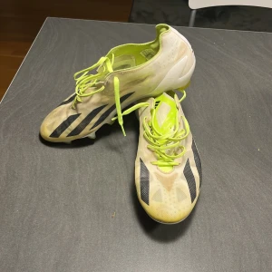 Fotbollsskor från Adidas - Säljer ett par fotbollsskor från Adidas i vitt och neongult med svarta detaljer. Skorna har snörning och är i välanvänt skick. Perfekta för fotbollsträning på gräs med sina dobbar för bra grepp.