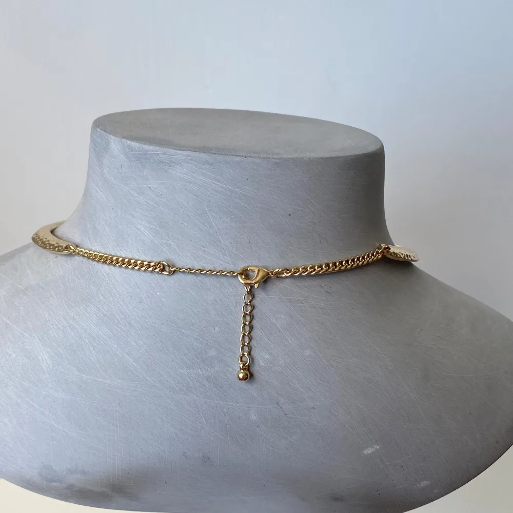 Säljer ett snyggt guldigt halsband med en cool hamrad yta. Det är ett choker-stil halsband som sitter nära halsen och har en justerbar kedja baktill för perfekt passform. Perfekt för att ge en elegant touch till vilken outfit som helst!. Accessoarer.