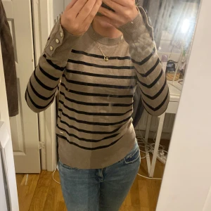 Beige randig stickad tröja  - Beige randig stickad tröja. Guld knappar i armarna. Jättebra skick, knappt använd. 