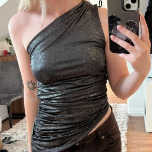 Svart/ silvrig fest topp - Säljer en superfin glittrig oneshoulder topp. Toppen är svart/ silver och är från H&m. Använd fåtal gånger, Storlek XS💕