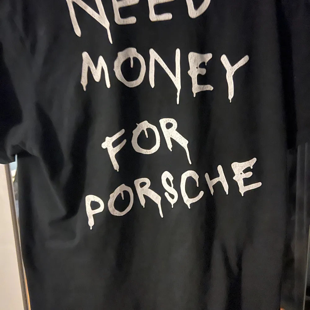 Säljer en svart t-shirt med texten 'NEED MONEY FOR PORSCHE' i vit. Den är kortärmad och har en normal passform. Perfekt för en avslappnad stil eller som ett roligt statement-plagg. Använd men i bra skick!. T-shirts.