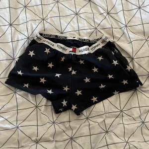 Svarta stjärnmönstrade shorts från Tommy Hilfiger - Säljer ett par svarta shorts från Tommy Hilfiger med vita stjärnor över hela tyget. De har en elastisk midja med Tommy Hilfiger-loggan runtom. Perfekta för en avslappnad dag eller sommarens alla äventyr!