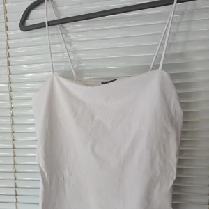 Vit linne från Gina Tricot - Enkelt och stilrent vitt linne från Gina Tricot. Linnet är gjort av 92% bomull och 8% elastan, både bekvämt och stretchigt.Axelbandslös design som ger en snygg och minimalist.Använt endast en gång,liten svag fläck förkommer dock!(sista bilden)