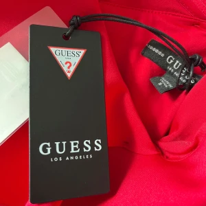 Röd klänning från Guess - Säljer en superfin röd klänning från Guess. Den har en elegant volangdetalj vid axlarna och är perfekt för festliga tillfällen. Klänningen är i storlek S och har en smickrande passform. Perfekt för att sticka ut på festen! Är helt ny och köpt i usa 🇺🇸 
