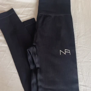 Svart ribbad tröja från NA - Säljer en snygg svart ribbad träning-set från NA. Perfekt för träning. Tröjan har långa ärmar och en normal passform. Dem är  gjorda iett mjukt och stretchigt material. Byxorna medföljer. Använt Ca 4-5 gånger inga synliga fel. Passar mig inte längre. 