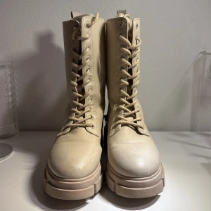 Beige boots med snörning och dragkedja - Snygga beige boots med grov sula och snörning framtill. De har även en praktisk dragkedja på sidan för enkel på- och avtagning. Perfekta för en trendig look.
