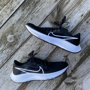 Svarta Nike löparskor - Snygga svarta Nike löparskor med vit sula och ikonisk swoosh-logga. Skorna har snörning och är perfekta för löpning och träning. Använda men inte slitna. Inga defekter