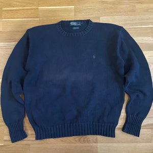 Mörkblå tröja från Polo Ralph Lauren - Säljer en stilren mörkblå tröja från Polo Ralph Lauren i 100% bomull. Tröjan har en broderad logotyp på bröstet och ribbade muddar vid ärmslut och nederkant. Perfekt för en klassisk look. Dessvärre missfärgning i mitten på framsidan.