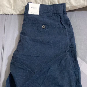 Blå linneblandade shorts från Dressmann - Snygga blå shorts i linneblandning från Dressmann. De har en dragkedja och knapp framtill samt ett stilrent mönster på insidan av linningen. Perfekta för varma dagar. Lappen kvar! Pris kan diskuteras