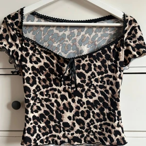 Leopardmönstrad topp - Snygg leopardmönstrad topp med korta ärmar och en söt knytning framtill. Toppen har en dekorativ kant vid halsringningen och är perfekt för en trendig look.