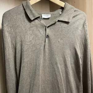 Beige pikétröja från Lindeberg - Säljer en stilren beige pikétröja från Lindeberg. Tröjan har långa ärmar och en klassisk krage med knappar. Perfekt för en avslappnad men ändå uppklädd look.