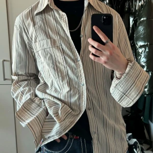 Vintage randig skjorta - En randig skjorta med långa ärmar. Skjortan har en ficka på bröstet och knappar framtill. I fint skick förutom en liten defekt på höger arm, se bild.  Mått: Axelbredd 46 cm Längd 75 cm Bröstkorg 55 cm Hemm 53 cm