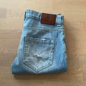 Ljusblå jeans från Dondup - Snygga ljusblå jeans från Dondup med slitna detaljer och knappgylf. De har en avslappnad passform och är perfekta för en casual look. Märkeslogga på baksidan ger en extra touch.