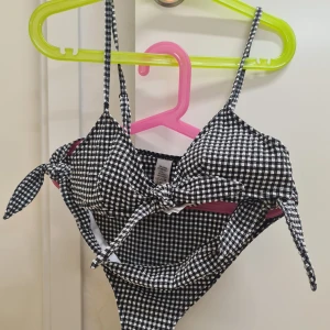 Svartvit rutig bikini XS & S - Söt bikini i svartvitt rutigt mönster med knytning fram. Toppen har smala axelband och en söt knutdetalj framtill. Underdelen har matchande knytband på sidorna. Bikini i XS och bikinitrosor i S. 