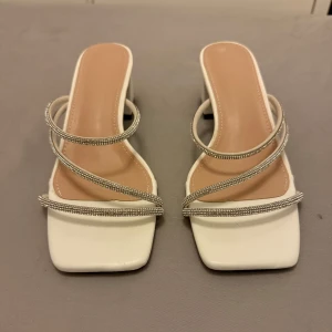Vita sandaler med glittriga remmar - Snygga vita sandaler med fyrkantig tå och glittriga remmar. Perfekta för en stilren look med en touch av glamour. Klackhöjd ger extra elegans.