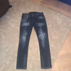 Mörkblå jeans från Dondup  - Snygga mörkblå jeans från Dondup med slitna detaljer och en klassisk femficksdesign. De har en knappgylf och är perfekta för en avslappnad stil. Modell - George Storlek 31. 
