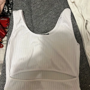 Vit ribbad linnetopp från Parisian - Säljer en stilren vit ribbad linnetopp från Parisian. Toppen har en unik design med en liten öppning framtill och är ärmlös. 