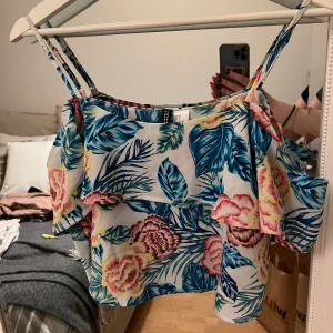 Blommig offshoulder topp från H&M - Säljer en färgglad blommig offshoulder topp från H&M. Toppen har volangdetaljer och smala axelband. 