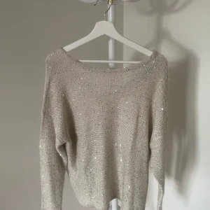 Beige stickad tröja med paljetter - Snygg beige stickad tröja med glittrande paljetter. V-ringad bak i ryggen. Köpt second hand