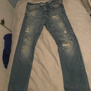 Blå jeans från Replay - Säljer ett par blå Replay jeans med slitna detaljer och en straight passform. Modellen är Jennon som är lite mer relaxed än anbass men sitter ändå mycket bra. Skriv vid frågor. Storlek 31/32