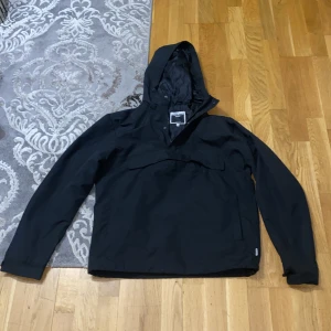 Svart jacka från Jack & Jones - Säljer en stilren svart jacka från Jack & Jones Core. Jackan har en praktisk huva och är långärmad, perfekt för kyligare dagar. Den är tillverkad i ett syntetmaterial och har en enkel design utan mönster.