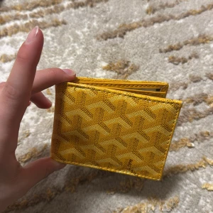 Gul plånbok med mönster - Snygg gul plånbok med ett unikt mönster. Den har flera fack för kort och sedlar, perfekt för att hålla ordning på dina tillhörigheter. Kompakt och stilren design som passar i fickan.