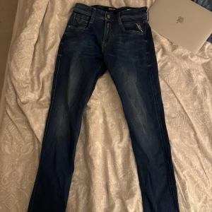 Blå jeans anbass från Replay - Helt oanvända Snygga blå anbass jeans från Replay med klassisk femficksdesign och knappgylf. Perfekta för en avslappnad stil med en modern touch. Märkeslappen på baksidan ger en extra detalj. 