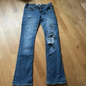 Blå bootcut jeans - Snygga blå bootcut jeans med slitningar på benen , Klassisk femficksdesign och knappgylf. från holister dom är super fina skicka vid minsta lilla fundering  går ned i pris
