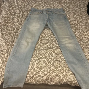 Ljusblå jeans från Levi's - Säljer ett par klassiska ljusblå Levi's 501 jeans. De har en rak passform och är tillverkade i denim med fem fickor och knappgylf. Perfekta för en avslappnad stil.