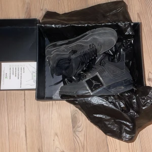 Svarta Nike Air Jordans - Säljer ett par svarta Nike Air Jordans med snörning och ikonisk design. Skorna har en robust sula och detaljerad ovandel i syntetmaterial. Perfekta för sneaker-entusiaster.