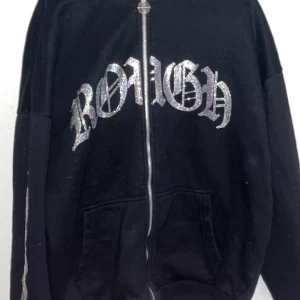 Svart hoodie med glittrig text - Snygg svart hoodie med dragkedja och glittrig text på framsidan. Perfekt för en cool och avslappnad stil. Har praktiska fickor framtill.