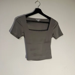 Grå kortärmad topp - Snygg grå topp med korta ärmar och fyrkantig halsringning. Perfekt för en stilren look.