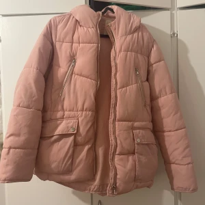 Rosa pufferjacka från Zara Girls - Säljer en söt rosa pufferjacka från Zara Girls. Jackan har en mysig huva och praktiska dragkedjor på fickorna. Perfekt för kyliga dagar.