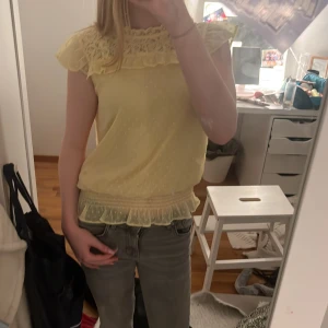 Gul blus med spetsdetaljer - Söt gul blus med spetsdetaljer vid halsen och volangkant nedtill. Perfekt för en somrig look. Blusen har korta ärmar och en luftig passform.