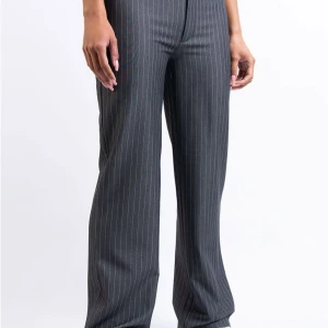 Grå randiga kostymbyxor från Monki - Snygga grå kostymbyxor från Monki med klassiskt randigt mönster. Byxorna har en rak passform som ger en stilren look. Perfekta för en chic och professionell stil. Första bilden är lånad!