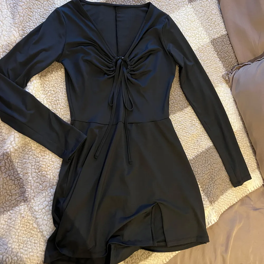 Snygg svart playsuit som ska se ut som klänning. Med långa ärmar och en ring i mitten av bröstet som man kan knyta. Klänningen har en slits i ena sidan. Knappt använd. Storlek S. från new Yorker.. Mekot.
